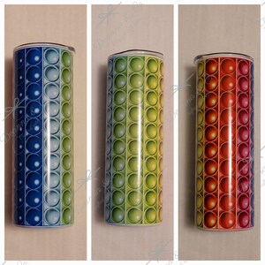 May include: Three stainless steel tumblers with a pop it design. The tumblers are blue and green, green and yellow, and red and orange.