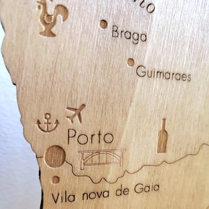 May include: A detailed wooden map of a region, featuring engraved city names like Porto, Braga, and Guimaraes. The map includes etched icons such as a rooster, airplane, anchor, bridge, and wine bottle, all in a natural wood finish.