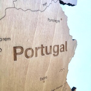 May include: A detailed wooden map of Portugal, with the country's name prominently displayed. The map features engraved geographical details, including cities like Portalegre and Evora, and the Tejo river. The wood has a natural, light brown color.