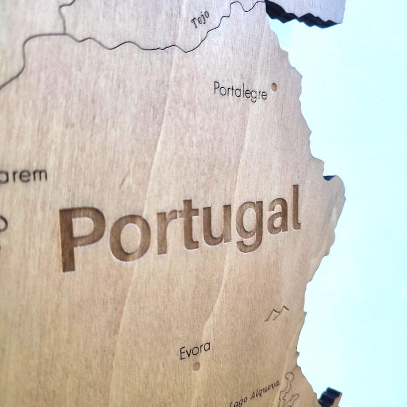 May include: A detailed wooden map of Portugal, with the country's name prominently displayed. The map features engraved geographical details, including cities like Portalegre and Evora, and the Tejo river. The wood has a natural, light brown color.