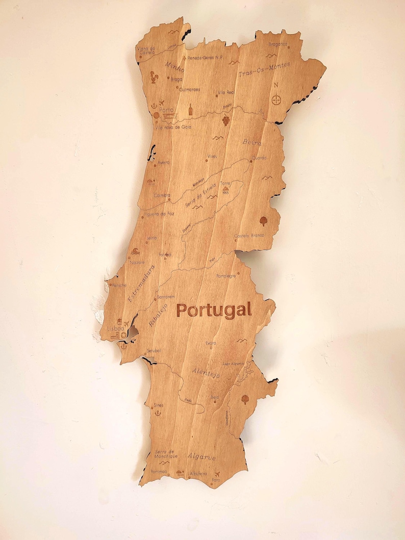 May include: A wooden map of Portugal, showcasing the country's outline and internal regions. The map is made of light-colored wood, with the country's name and regions labeled in a dark brown font. The map includes cities and landmarks.