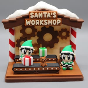 May include: A festive Christmas decoration featuring a miniature Santa's Workshop scene. The brown structure has a sign that reads "SANTA'S WORKSHOP". Two elves stand near a conveyor belt with gifts and a teddy bear. Red and white striped columns support the roof.