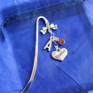 May include: Silver bookmark with a charm that says "Friend" and a letter "A" charm. The bookmark is in a blue mesh bag.