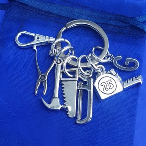 May include: Silver keychain with a variety of tools, including a hammer, saw, pliers, and a tape measure with the number 25 on it.
