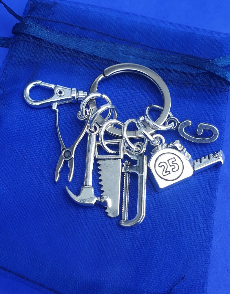 May include: Silver keychain with a variety of tools, including a hammer, saw, pliers, and a tape measure with the number 25 on it.