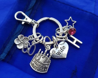 May include: Silver keychain with charms including a heart with the word "Wife", a cake with candles that says "Happy Birthday", a flower with the number 60, a star, a letter H, and a pink rhinestone.