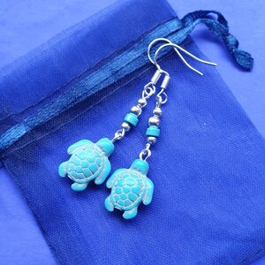 May include: A pair of turquoise sea turtle dangle earrings with silver beads and hooks. The earrings are on a blue background.
