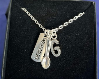 May include: A silver necklace with multiple charms, including a spoon, a tag that says "Warrior", and a letter "G". The necklace is displayed in a black box.