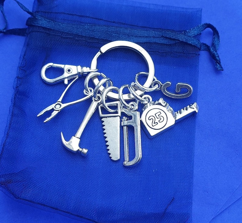 May include: A silver keychain with a variety of tools, including a hammer, saw, and a tape measure. The tape measure has the number 25 printed on it.