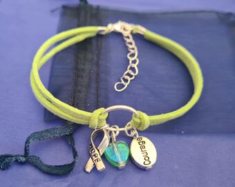 May include: A green suede bracelet with a silver charm that says "Courage" and a silver charm with a blue and green heart. The bracelet also has a silver ribbon charm with the word "Hope" on it.