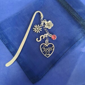 May include: Silver bookmark with a heart charm that says "Sweet 21" and other charms including a flower, a letter S, and a pink rhinestone.