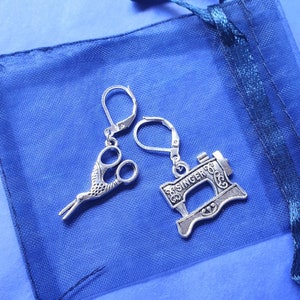 May include: A pair of silver earrings with a sewing machine and a pair of scissors charm. The earrings are on a blue mesh bag.