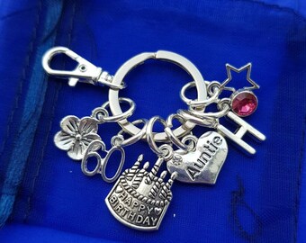 May include: Silver keychain with charms including a cake with candles, a heart with the word "Auntie" on it, a flower, the number 60, a star with a pink rhinestone, and the letter H.