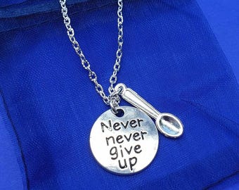 May include: Silver necklace with a round pendant that says "Never never give up" and a small spoon charm. The necklace is on a blue background.