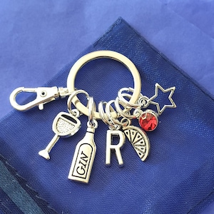 May include: Silver keychain with charms including a wine glass, a bottle with the word "GIN" on it, a letter "R", a lemon slice, a red rhinestone, and a silver star.