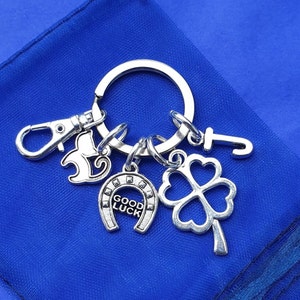 May include: Silver key chain with multiple charms, including a horseshoe with the words "Good Luck", a four-leaf clover, a cat, and a letter "J".