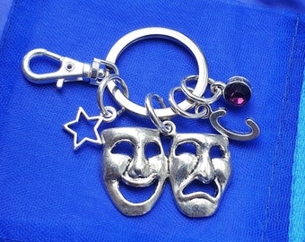 May include: Silver key chain with a star, two silver theatrical masks, a silver letter C charm, and a purple crystal charm.