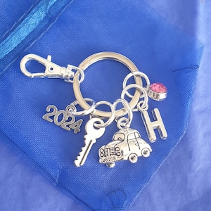 May include: Silver keyring with a key, a car charm, a pink rhinestone, a 2024 charm, and a letter H charm.