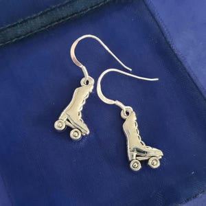 May include: A pair of silver roller skate earrings. The earrings are in the shape of a roller skate with four wheels. The earrings are hanging from silver hooks.