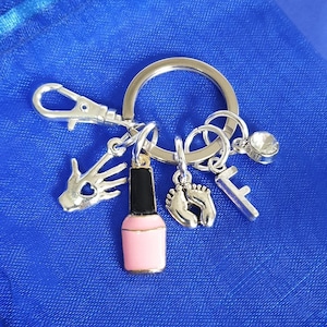May include: A silver keychain with a variety of charms, including a pink nail polish bottle, a pair of tiny feet, a hand with a heart, a letter F, and a clear rhinestone.