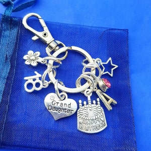 May include: Silver keyring with charms including a heart that says "Grand Daughter", a birthday cake with candles, a star, a flower, and a letter "A".