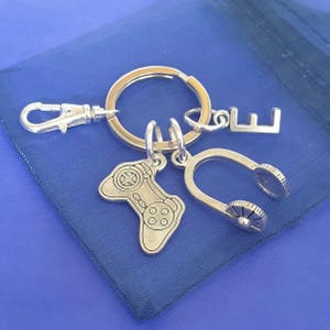 May include: Silver keychain with a video game controller charm, a headphone charm, and a letter E charm.