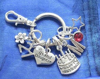 May include: Silver keyring with charms including a heart that says "Grand Daughter", a birthday cake, a star, a flower, a letter "M", and a red rhinestone.
