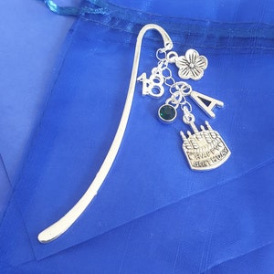 May include: Silver bookmark with a silver flower charm, a silver letter A charm, a silver number 18 charm, a green gem charm, and a silver cake charm with the text "Happy Birthday".