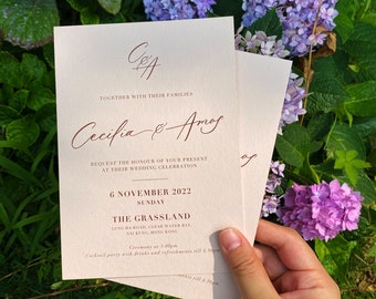 Può includere: Un invito di nozze con sfondo crema e testo marrone. La carta presenta i nomi "Cecilia & Amos" e la data "6 novembre 2022". L'invito è per una cerimonia di nozze e un ricevimento al The Grassland, Lung Ha Road, Clear Water Bay, Sai Kung, Hong Kong.