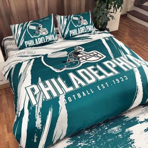Könnte beinhalten: Ein teal-weißes Philadelphia Eagles Bettwäsche-Set mit einem Footballhelm-Motiv und dem Teamnamen. Das Set enthält einen Bettbezug und zwei Kissenbezüge. Die Worte "PHILADELPHIA" und "FOOTBALL EST. 1933" sind auf dem Bettbezug aufgedruckt.