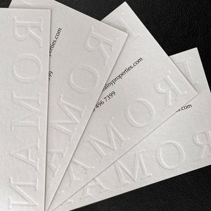 May include: Several white business cards are fanned out, displaying the embossed word "ROMOR". The cards also feature contact details, including a website address and a phone number.