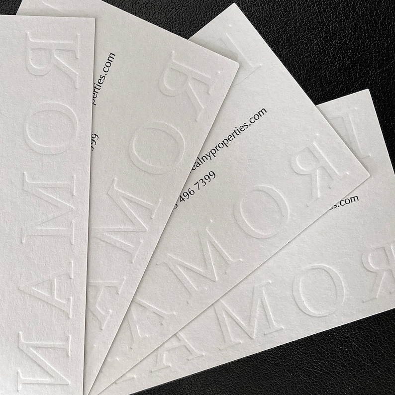 May include: Several white business cards are fanned out, displaying the embossed word "ROMOR". The cards also feature contact details, including a website address and a phone number.