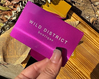 May include: A pink metal gift card with the text "WILD DISTRICT boutique" in white lettering.