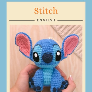 K&ouml;nnte beinhalten: Eine blaue Stitch-Puppe aus H&auml;kelarbeit mit gro&szlig;en Ohren, schwarzen Augen und einer dunkelblauen Nase. Die Puppe wird in den H&auml;nden einer Person gehalten. Das Wort "Stitch" steht in orangefarbener Schrift &uuml;ber dem Wort "ENGLISH". Das Catartist-Logo befindet sich oben links.