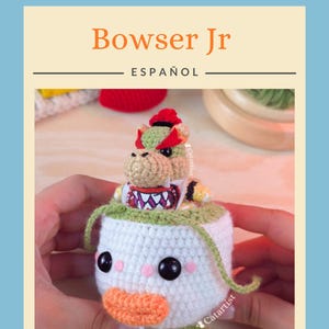 Op de afbeelding: Een gehaakte Bowser Jr. figuur, met een witte body, groene en oranje afwerking, zwarte ogen, roze wangen en een oranje snavel. De teksten "Bowser Jr" en "ESPA&Ntilde;OL" zijn zichtbaar. Het Catartist-logo is ook aanwezig.