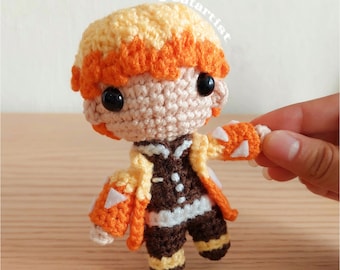May include: A crocheted plush toy of a character with yellow and orange hair, wearing a brown and yellow jacket with white accents. The toy has black eyes and a brown and white outfit.