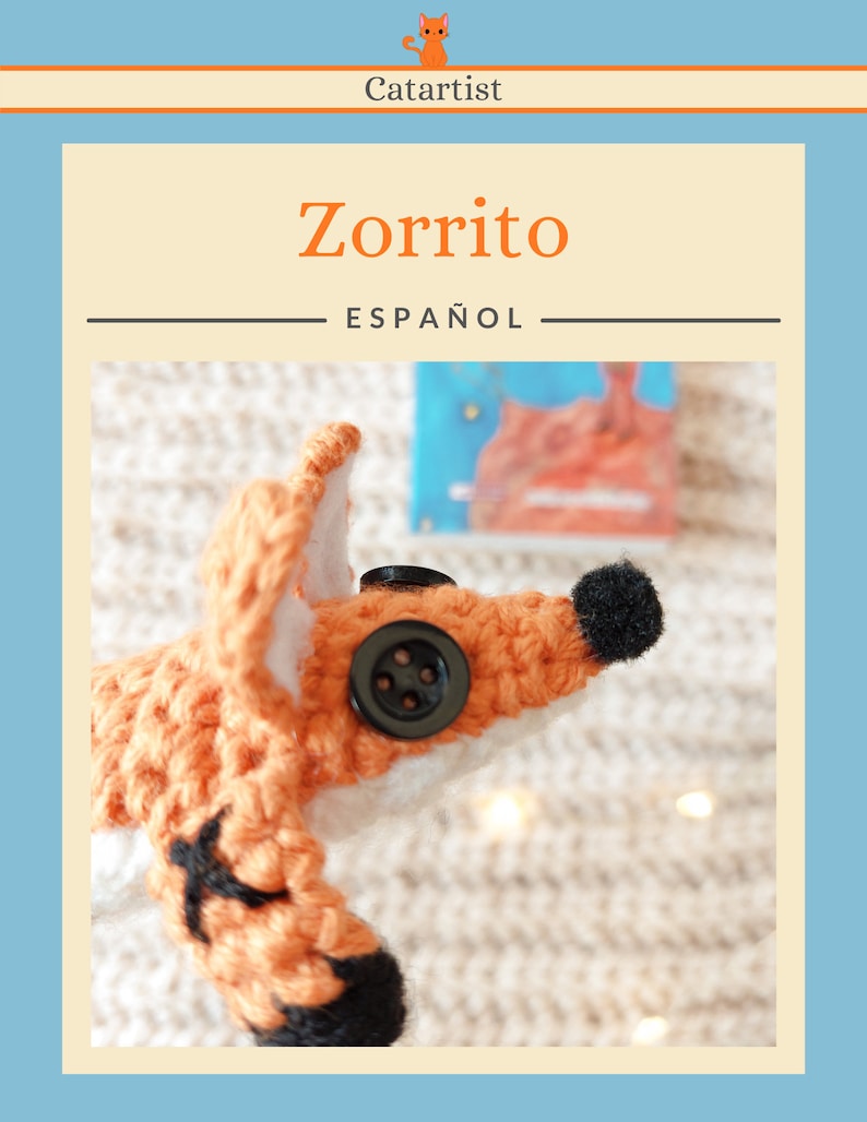 May include: A crocheted fox toy with black eyes and a black button nose. The fox is orange and white and has black accents on its paws and ears. The fox is lying on a white fuzzy surface.