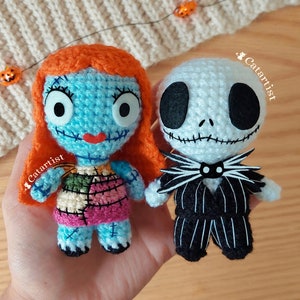 Puede incluir: Muñecas amigurumi de crochet de Sally y Jack Skellington de Pesadilla antes de Navidad. Sally es azul con cabello naranja y un vestido de retazos. Jack es blanco con rayas negras y una pajarita negra.