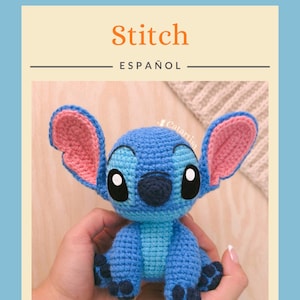 K&ouml;nnte beinhalten: Geh&auml;kelte blaue Stitch-Puppe mit gro&szlig;en Ohren und schwarzen Augen. Die Puppe wird in den H&auml;nden einer Person gehalten. Das Wort "Stitch" ist orange geschrieben, darunter das Wort "ESPA&Ntilde;OL". Das Catartist-Logo befindet sich oben links.