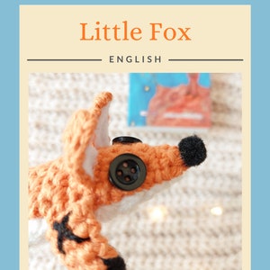 May include: A crocheted fox toy with black eyes and a black button nose. The fox is orange and white and is lying on a white knitted blanket.