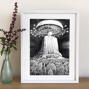 May include: A black and white pencil drawing of a large rock formation with a flying saucer hovering above it. The rock formation is surrounded by trees. The drawing is framed in a white frame.