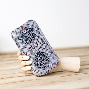 May include: A small, blue and white patterned fabric pouch with a wooden button closure. The pouch is held by a wooden hand.