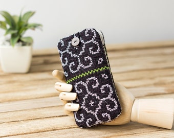 May include: A black and white phone case with a green trim and a button closure. The case is made of a woven fabric with a geometric pattern.
