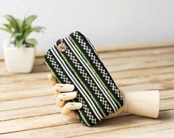 May include: A black and green striped fabric pouch with a wooden button closure. The pouch is held by a wooden hand.