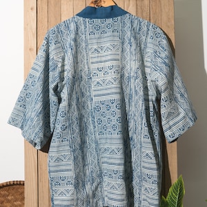 May include: A blue and white patterned kimono with a tie closure. The kimono is hanging on a wooden hanger against a wooden background.