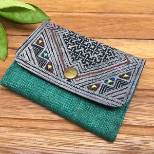May include: A small, green and gray wallet with a geometric pattern and a metal button. The wallet is made of fabric and has a flap closure.