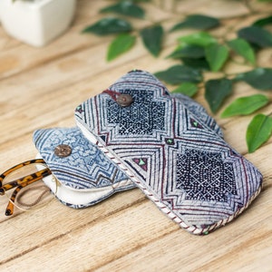 May include: Two blue and white patterned fabric eyeglass cases with a brown tortoiseshell pair of glasses inside one of the cases. The cases are on a wooden surface.