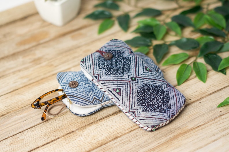 May include: Two blue and white patterned fabric eyeglass cases with a brown tortoiseshell pair of glasses inside one of the cases. The cases are on a wooden surface.