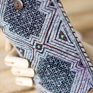 May include: A close-up of a blue and white patterned fabric phone case with a red and white trim. The case has a geometric design with small white dots and a button on the top.