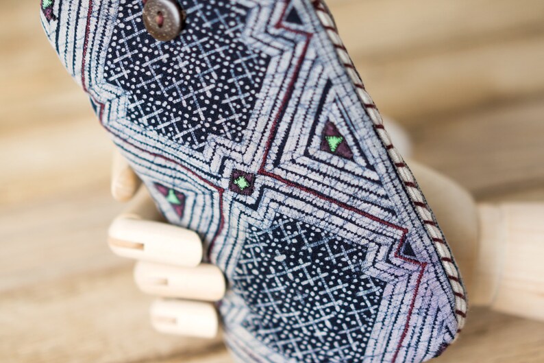 May include: A close-up of a blue and white patterned fabric phone case with a red and white trim. The case has a geometric design with small white dots and a button on the top.